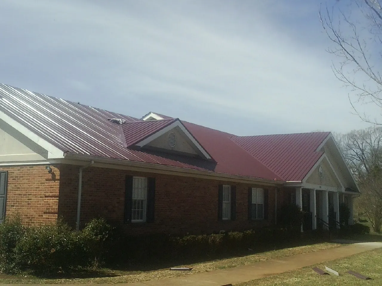 Red metal roof with gabled entries on a long brick building, from a Hail Damage Roof Repair job in Tate