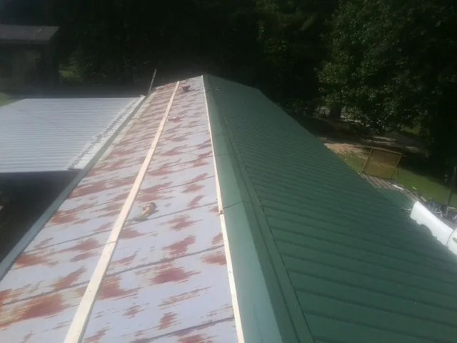 Old rusted panels beside newly installed green metal roofing — Wind Damage Roof Repair by Roofing Brothers in Tate