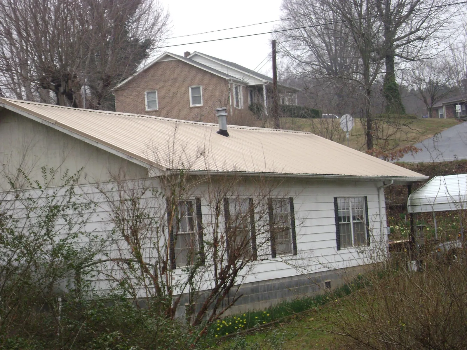 Tan metal roof on a white sided house set into a hillside — Commercial Roofing by Roofing Brothers in Tate